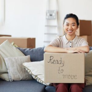 image shows a woman sitting on a couch holding a box that says "ready to move"
